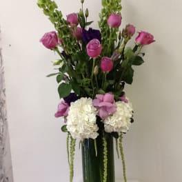 Tall bouquet of pink roses, white hydrangeas, and green hanging accents in a glass vase