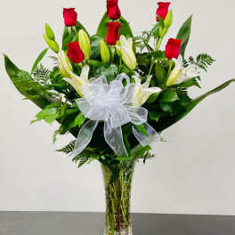 Red roses and white lilies in a clear glass vase with a white bow