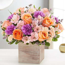 Peach and purple flower arrangement in a wooden box