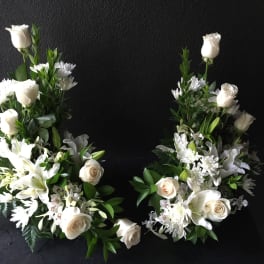 Two white floral sprays with roses and lilies arranged in a heart shape