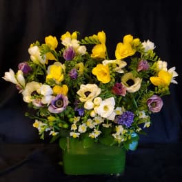 Yellow, white, and purple flowers arranged in a green vase