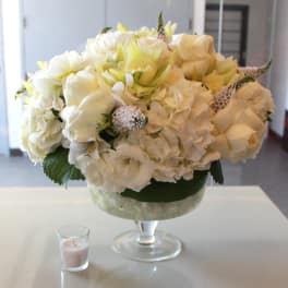 Cream and white floral arrangement in a glass pedestal vase