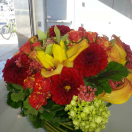 Bright mixed bouquet with red dahlias, yellow calla lilies, and pink blooms in a glass vase