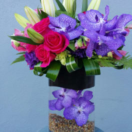 Bouquet of pink roses, lilies, and purple orchids in a glass vase