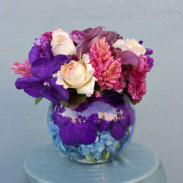 Purple and pink floral arrangement in a round glass vase