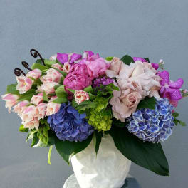Mixed pink, purple, and blue flowers arranged in a white vase