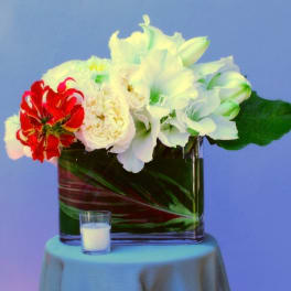 White and red flowers arranged in a square glass vase with a small candle in front