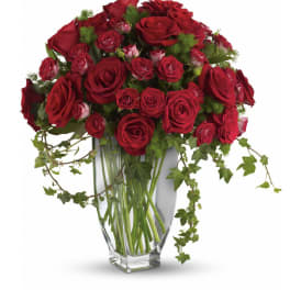 Red roses arranged in a clear glass vase with trailing ivy