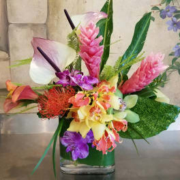 Tropical flower arrangement with orchids, calla lilies, and pink ginger in a glass vase