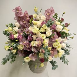 Large arrangement of cream and mauve roses with pink orchids in a gray ceramic pot