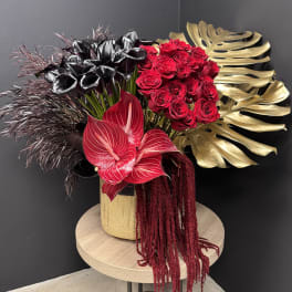 Dramatic arrangement of red roses, black calla lilies and tropical blooms in a gold vase with gold leaves
