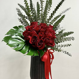 Tall black vase with red roses, large tropical leaf, and radiating eucalyptus stems.