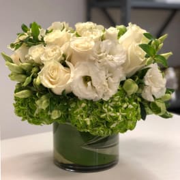 Low arrangement of white roses and lisianthus with green hydrangea in a glass cylinder vase
