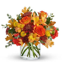 Autumn bouquet of orange roses and mixed flowers in a clear glass vase