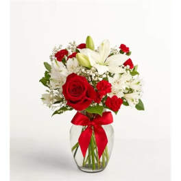 Red roses and white lilies in a clear glass vase with a red ribbon