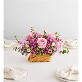 Pink and purple flower arrangement in a woven basket on a table