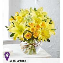 Yellow lilies and roses arranged in a clear glass vase