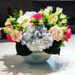 Mixed bouquet of roses, hydrangeas, and lilies in a round vase