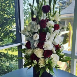 Tall arrangement of red and white roses with white blooms in a dark vase