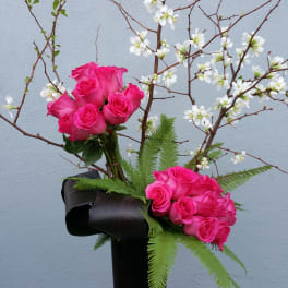Pink roses in a tall black vase with white blossoms on branches
