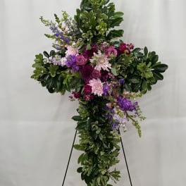Large cross-shaped floral tribute with purple and pink flowers on a stand