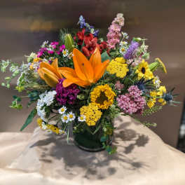 Colorful mixed bouquet with orange lilies and sunflowers in a dark vase