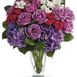 Purple and pink rose bouquet with white blooms in a clear glass vase