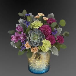 Succulent and mixed flower arrangement in a blue and gold glass vase