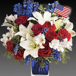 Red roses and white lilies in a blue glass vase with a small American flag
