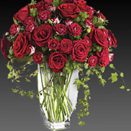 Red rose bouquet in a clear glass vase with trailing greenery