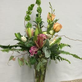 Tall mixed floral arrangement in a clear glass vase with peach roses and pink blooms