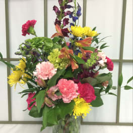 Colorful mixed bouquet in a clear glass vase with pink, yellow, purple, and orange blooms