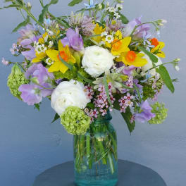Mixed bouquet of yellow, purple, and white flowers in a glass jar vase