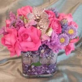 Pink and purple bouquet in a square glass vase with spotted orchids