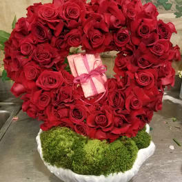 Heart-shaped red rose arrangement with a pink gift box in the center