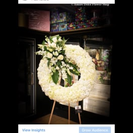 White floral funeral wreath on a wooden easel with lilies and roses