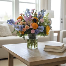 Mixed bouquet of pastel flowers in a glass vase on a coffee table