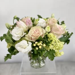 Pastel roses and white blooms arranged in a clear glass vase