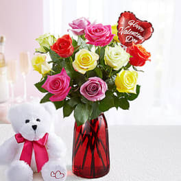 Bouquet of multicolored roses in a red vase with a teddy bear beside it