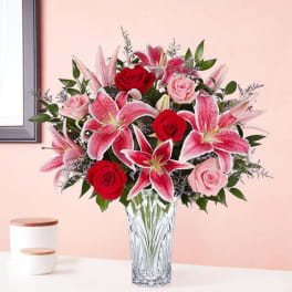 Bouquet of pink lilies and red and pink roses in a clear glass vase