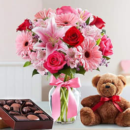 Pink and red mixed bouquet in a glass vase with a teddy bear and chocolates