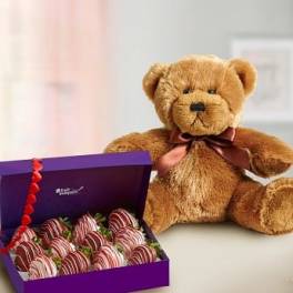 Brown teddy bear beside an open purple box of chocolate-covered strawberries