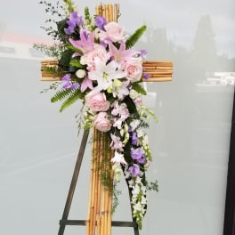 Floral cross arrangement with pink and purple flowers on a bamboo cross stand