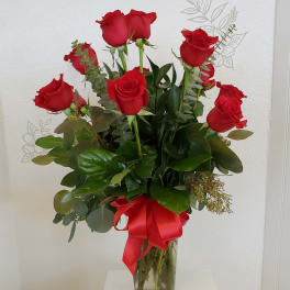 Red roses arranged in a clear glass vase with a red ribbon.