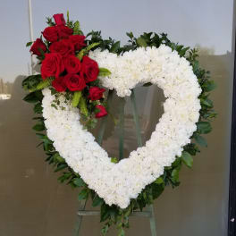 Heart-shaped floral wreath with white blooms and red roses on an easel