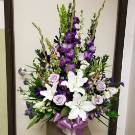 Tall floral arrangement with white lilies, purple roses, and purple spikes in a vase