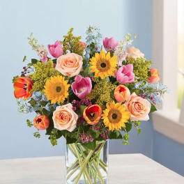 Mixed bouquet of roses, tulips, and sunflowers in a clear glass vase