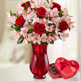 Red roses and pink lilies in a red vase beside a heart-shaped chocolate box