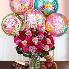 Bouquet of roses in a glass vase with Mother’s Day balloons, chocolates, and a teddy bear