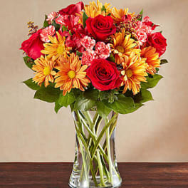 Red roses and orange daisies in a clear glass vase